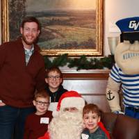 An alumnus and his three sons sitting with Santa.